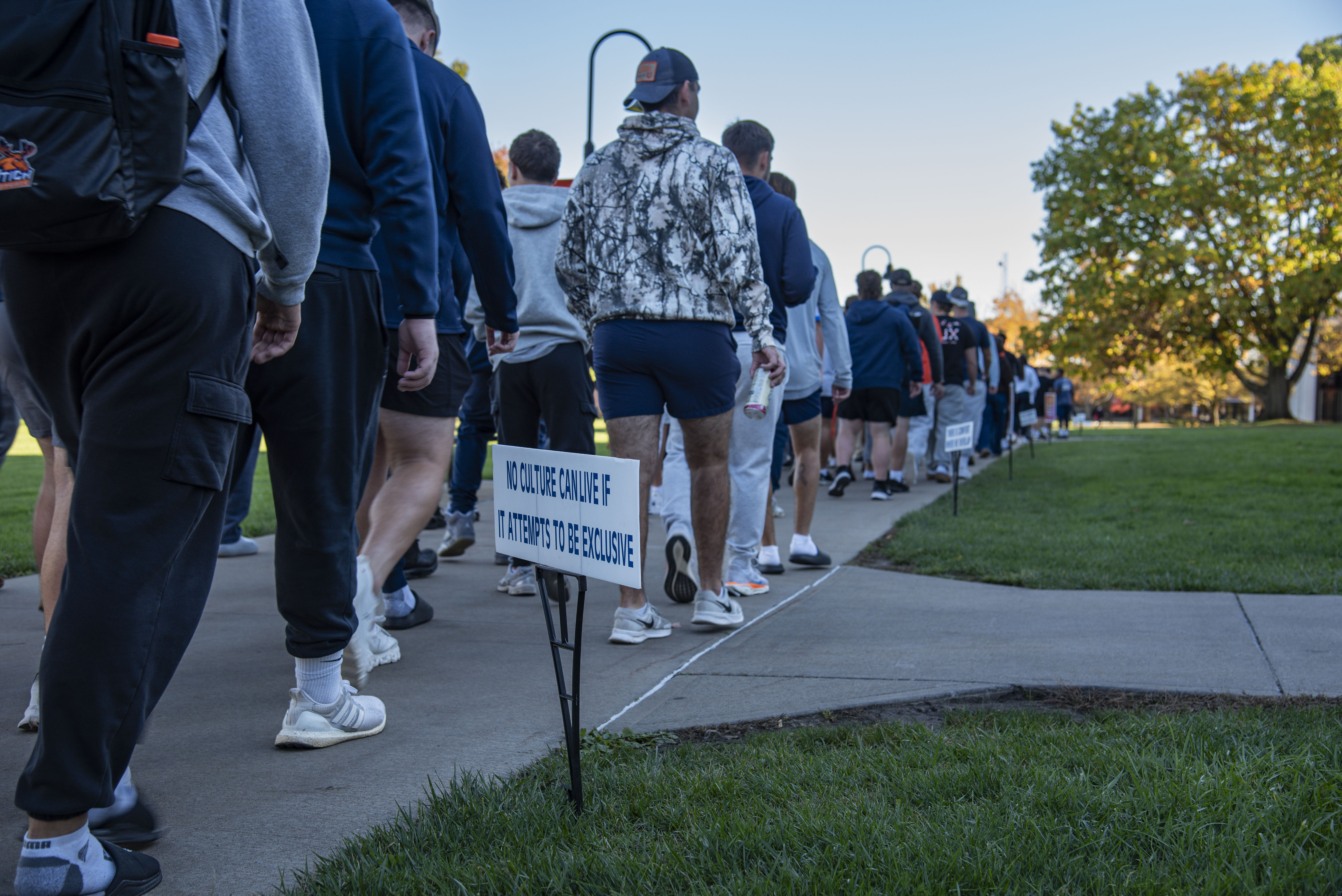 A line of students, faculty, and staff walk away from the camera and across campus.