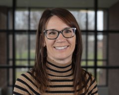 Renee Fisher in glasses and a striped turtleneck stands in front of a window.