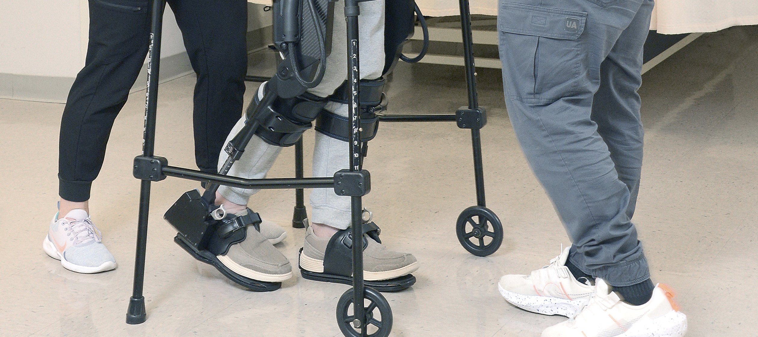 Close-up of patient's legs and hands using walker with assistance.