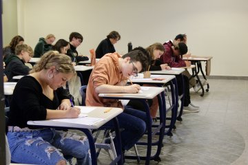 Students at desks, writing on paper as they take part in the AMC 10/12 Mathematics Competition.