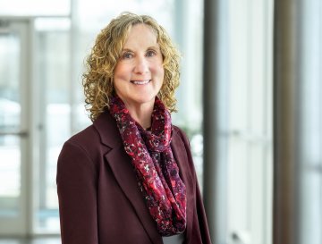 Dr Ann Damiano, in a purple blazer and scarf, stands by glass windows.