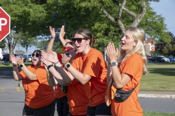 Students in orange t-shirts clap and shout happily for newcomers to campus.