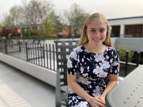 Isabelle LaBelle '23, in floral dress, sits at a table in the courtyard outside the library.