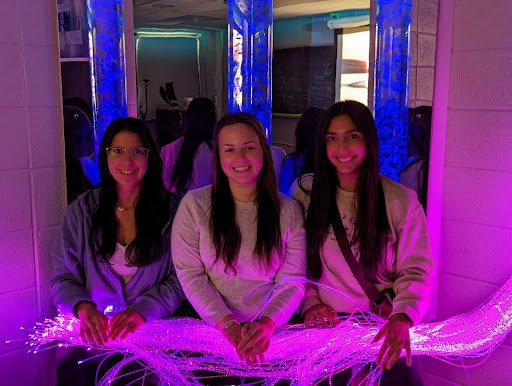 Three students sit in the Utica University Sensory Room, with purplish-blue lights on.