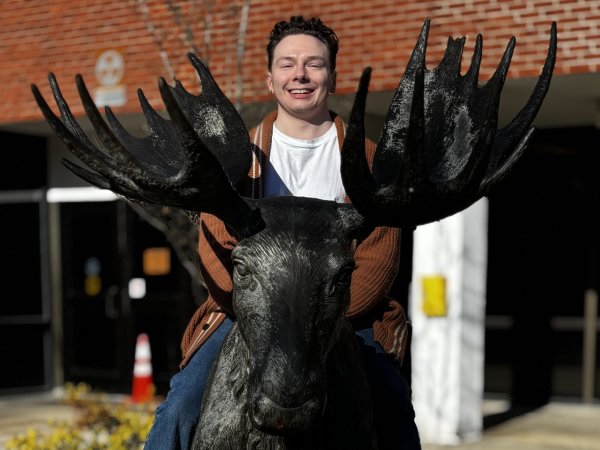 Marshall Hildreth '26 sits on top of a moose sculpture outside a brick building.