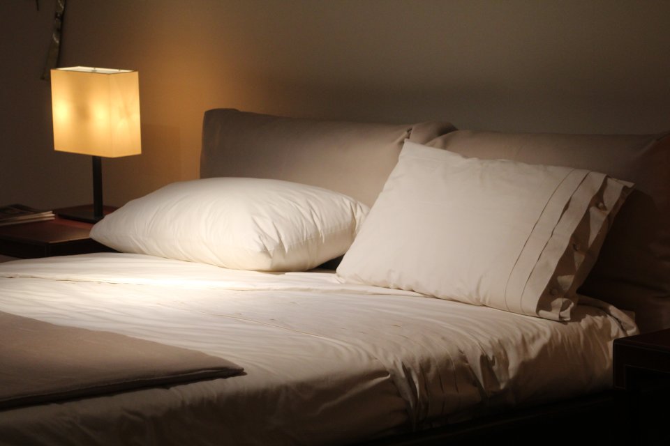 Pillows on a Bed in Dark Room with lamp light.