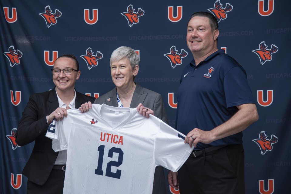 Kristin St. Hilaire, Stephanie Nesbitt, and Damian Boehlert hold up a Utica Pioneers jersey.